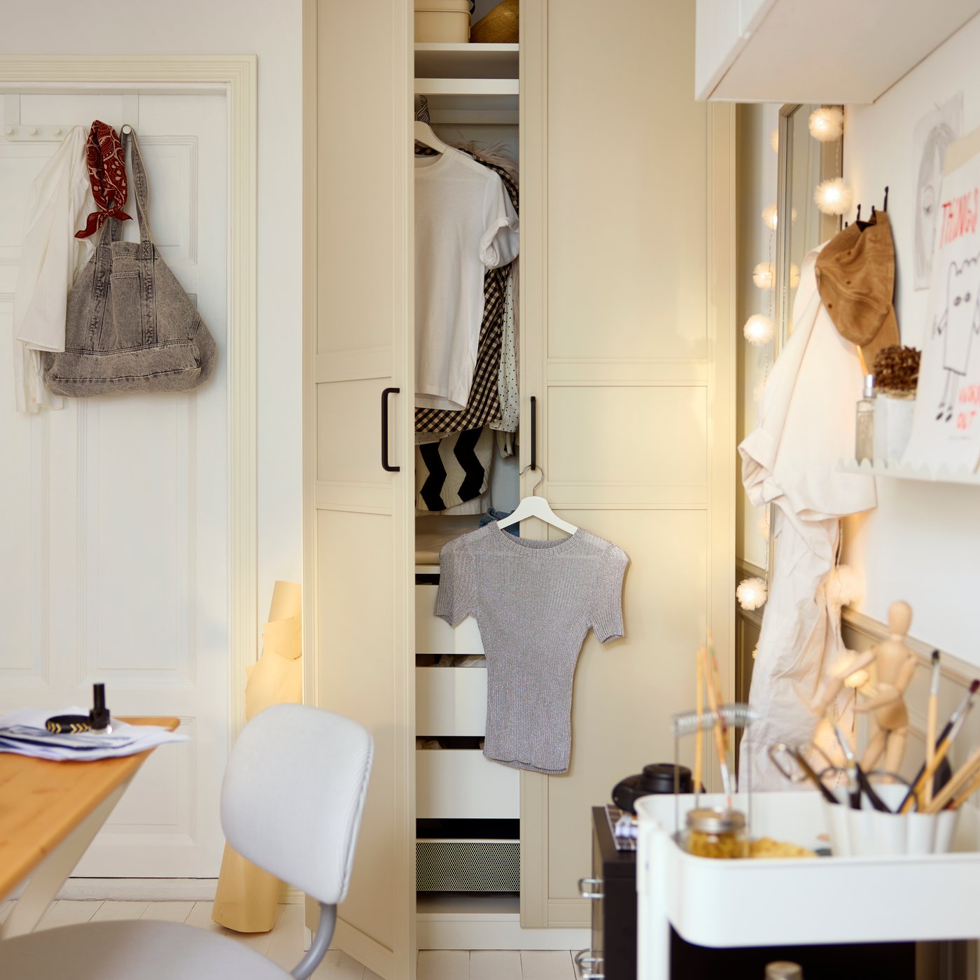 Closet area with a light beige FLISBERGET door revealing open compartments with clothes, next to a workspace.