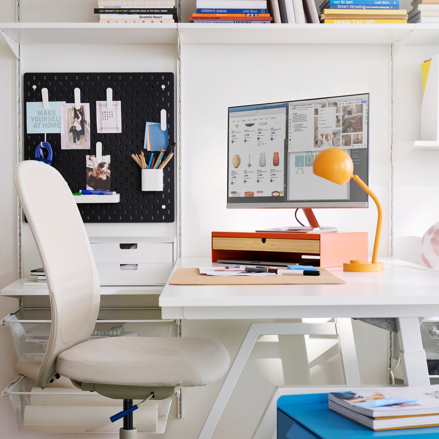 A workspace featuring a bright orange ELLOVEN monitor stand with a drawer on a white desk with a stylish chair.