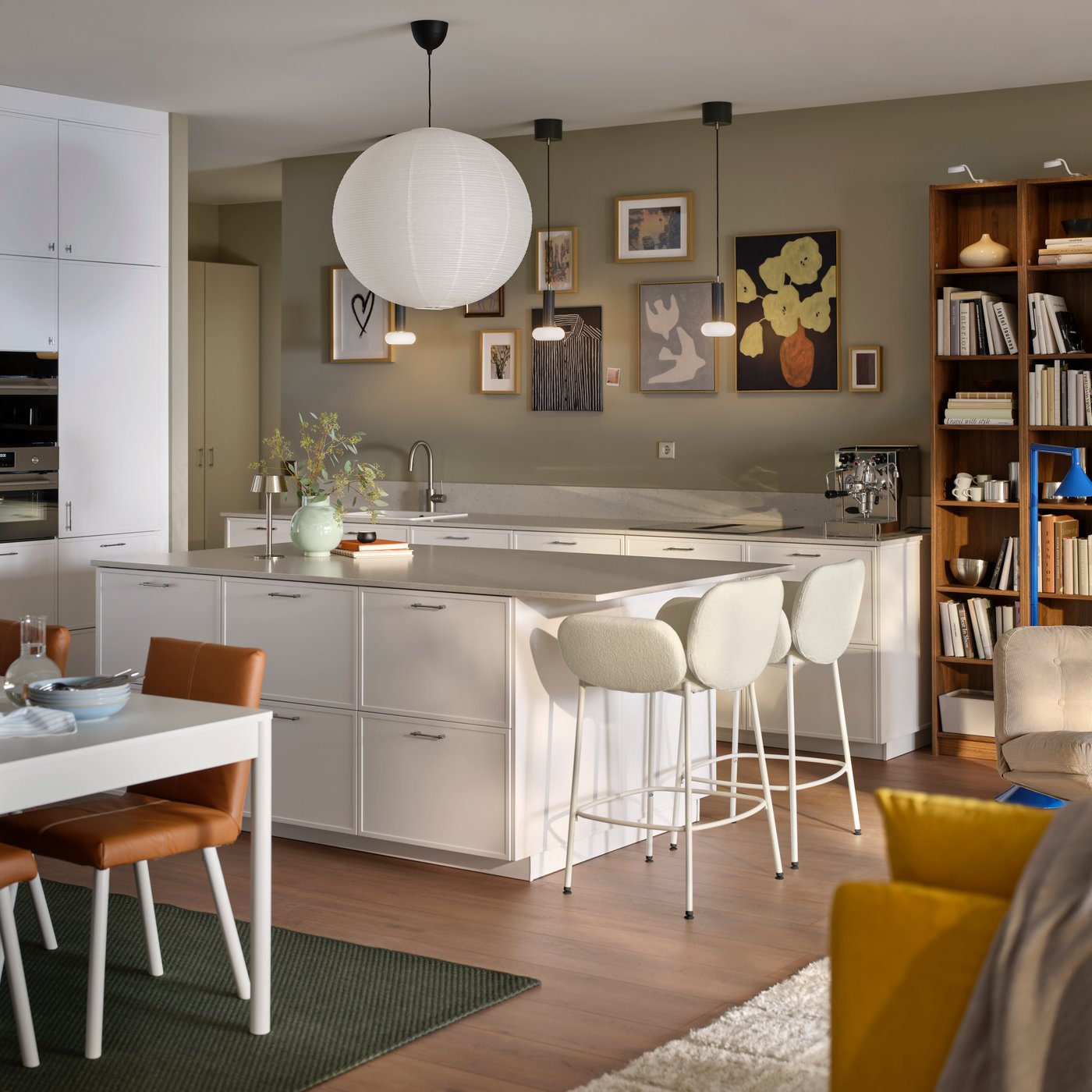 A modern kitchen with white ASPUDDEN fronts featuring a kitchen island and SYNTORP bar stools connecting to the living room.