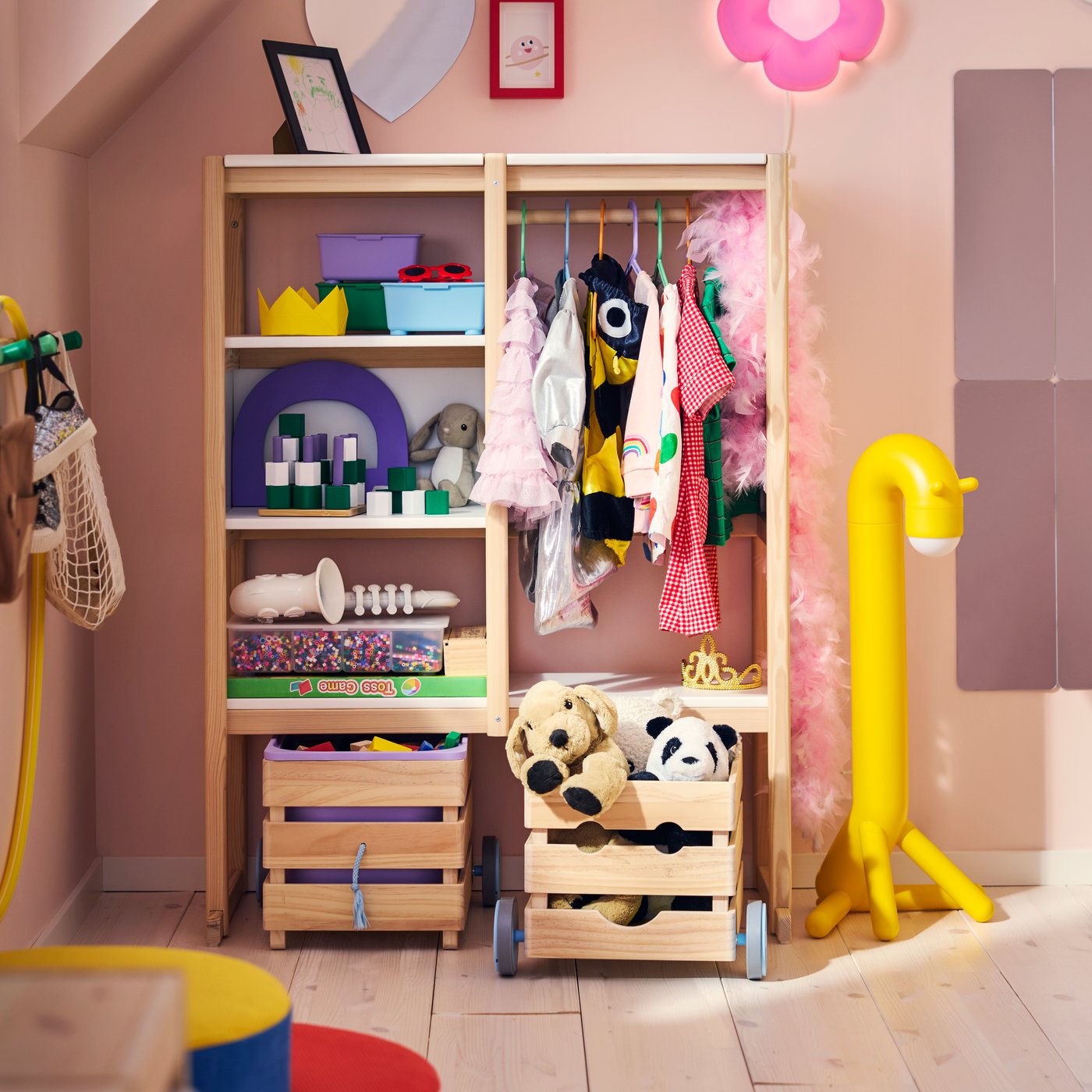 A pink children’s room with a FLISAT open storage with shelves, a clothes rail with dress-up clothes and wheeled boxes.